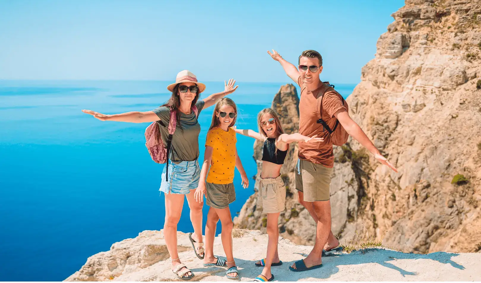 Family standing on a cliff with arms outstretched, enjoying the sea view